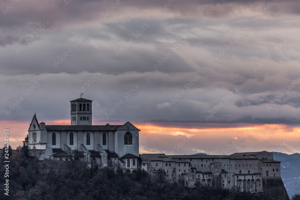 Beautiful view of St.Francis church in Assisi town (Umbria, Italy) from an unusual place at sunset, with moody clouds in the sky