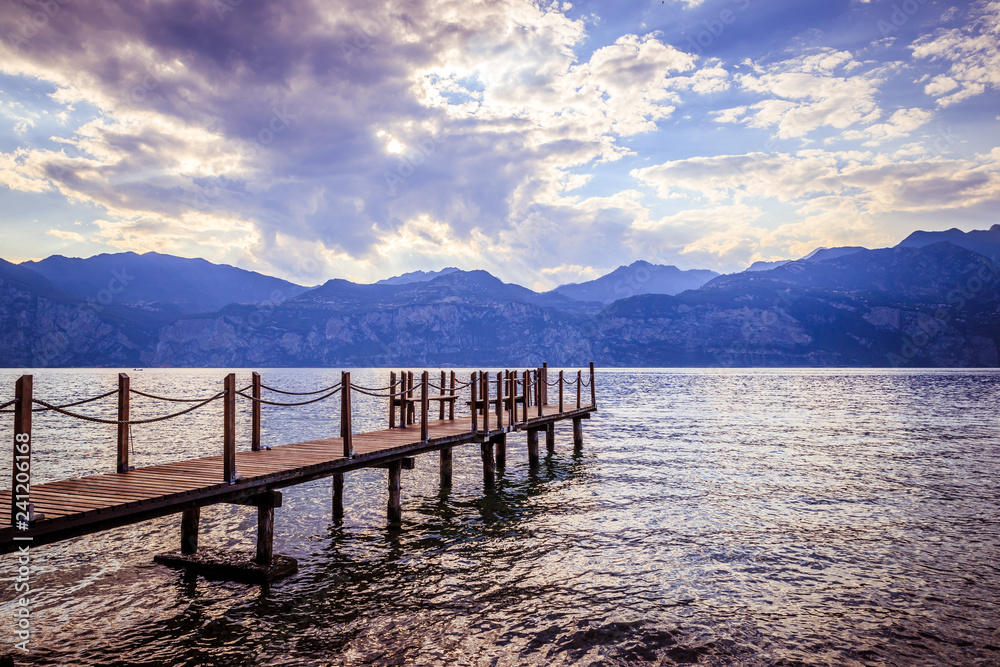 Scenery with wooden dock pier extending over blue lake water and mountains