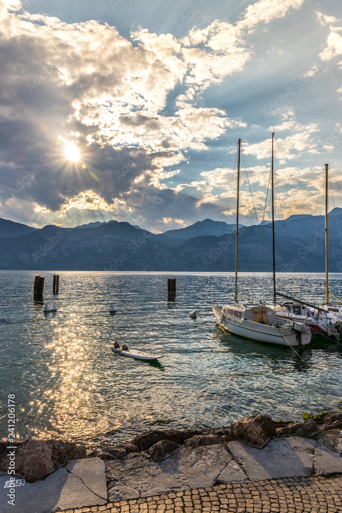 Sailing boats at an italian lake, sunset, mountains and clouds