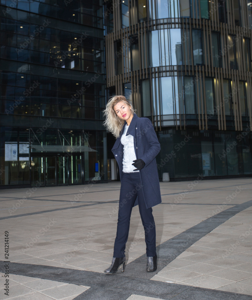 Pretty young blonde woman in coat outside business center.