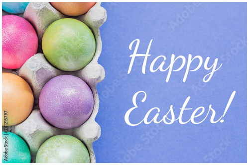 Multicolored easter eggs in a box on blue background, Top view. Greeting card Happy Easter