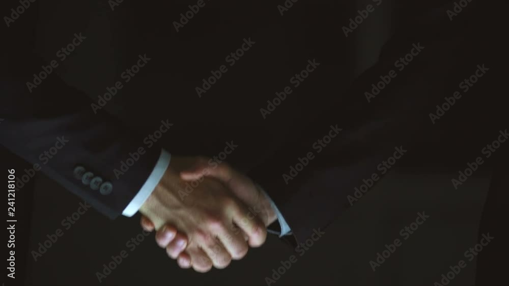 The two male handshake on the dark background. slow motion