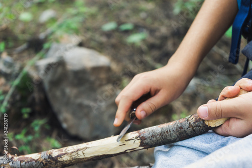 Mano de un niño con navaja quitando corteza rama en bosque photo