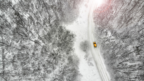 Aerial. Beautiful rural country road between forest with yellow car in winter season. © Dmytro