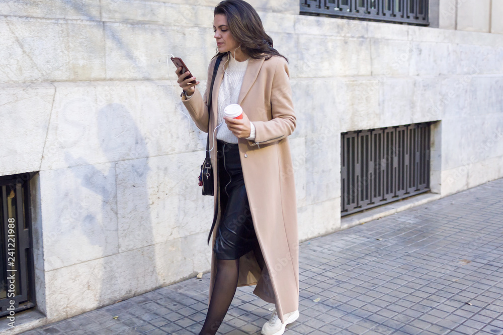 Pretty young woman using her mobile phone while walking in the street.