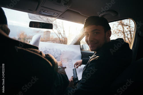 фотографія Two violent robbers sitting in a car looking at a blueprint of the building they want to rob while proudly showing off their guns