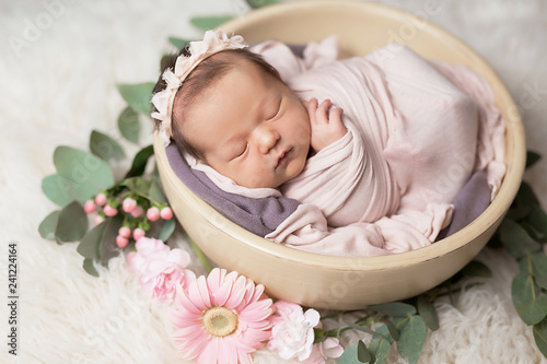 Cute newborn little girl sleeping in crib with flowers. Baby goods packaging template. Closeup portrait of newborn baby with smile on face. Healthy and medical concept. 