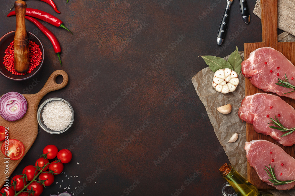 Pieces of raw pork steak on cutting board with cherry tomatoes, rosemary, garlic, red pepper, bay leaf, onion, salt and spice mortar on rusty brown background Pieces of raw pork steak on cutting board with cherry tomatoes, rosemary, garlic, red pepper, bay leaf, onion, salt and spice mortar on rusty brown background