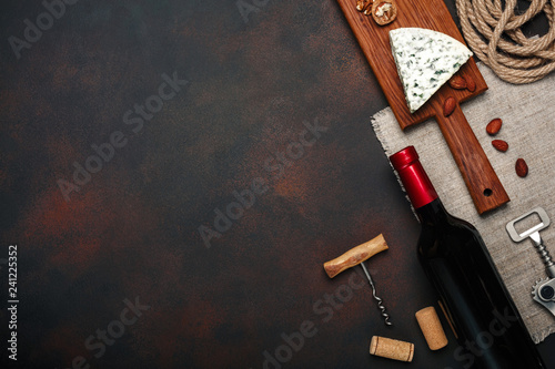 Bottle of wine, walnut, blue cheese, almonds, corkscrew and corks, on rusty background top view