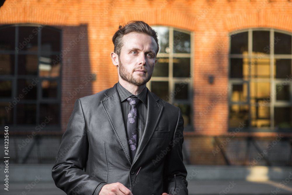 Half length portrait of young confident man manager standing outside of his office building, prosperous male leader dressed in suit after business meeting Half length portrait of young confident man manager standing outside of his office building, prosperous male leader dressed in suit after business meeting