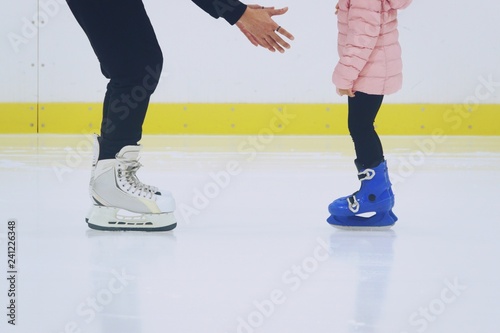 father teaching daughter to skate at ice-skating rink