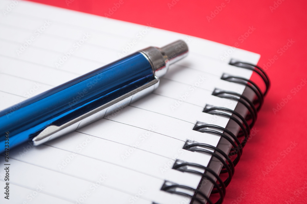 closeup of blue pen on spirales note book on red background closeup of blue pen on spirales note book on red background