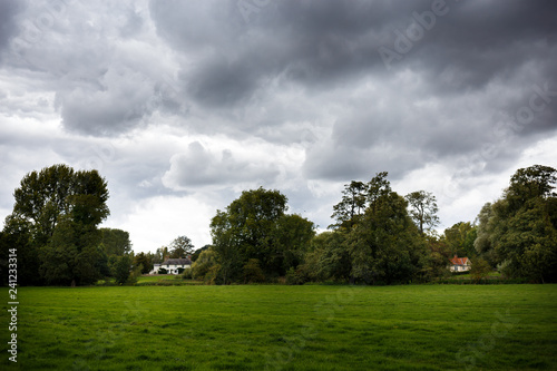 water meadows lined with trees with cloudy sky and cottages