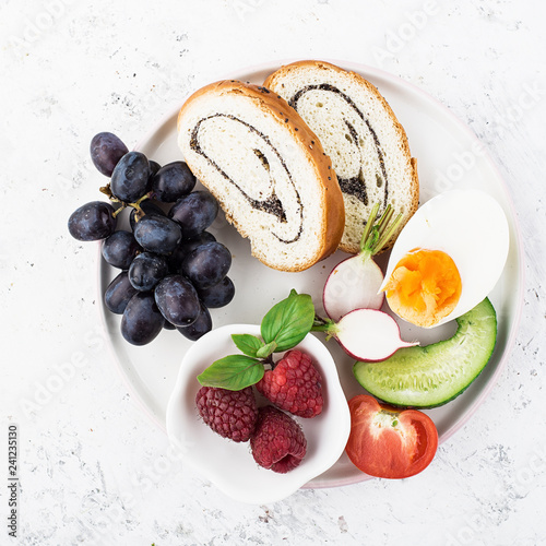 A healthy farmer family breakfast snack. Slices of cereal bread with nuts, poppy rolls, halves of boiled egg, cucumber, radish, fresh juicy vegetables and berries. Top View.