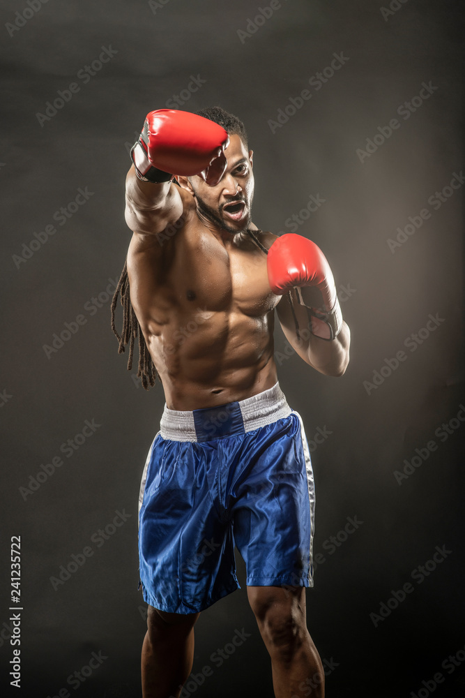 Muscular African American Black male sweaty boxer does an agressive punch towards the camera  with dramatic lighting with a black background  