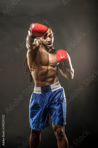 Muscular African American Black male sweaty boxer does an agressive punch towards the camera with dramatic lighting with a black background 