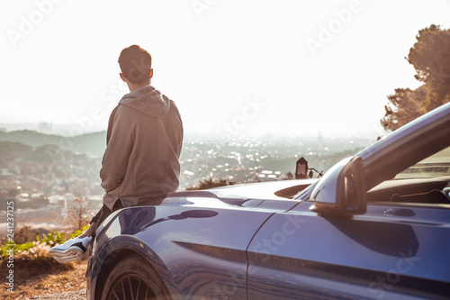 Guy sitting in luxury sports car at viewpoint at sunrise