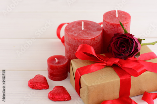 Fototapeta Naklejka Na Ścianę i Meble -  Valentines day red background with red roses on a white wooden table. A gift box decorated with hearts and candles on the table.