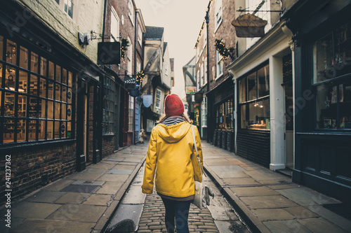 A rear view of a girl in a yellow coat walking along the historic street known as The Shambles in York, UK which is a popular tourist destination and medieval landmark in this ancient city photo