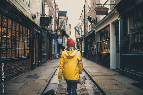 A rear view of a girl in a yellow coat walking along the historic street known as The Shambles in York, UK which is a popular tourist destination and medieval landmark in this ancient city