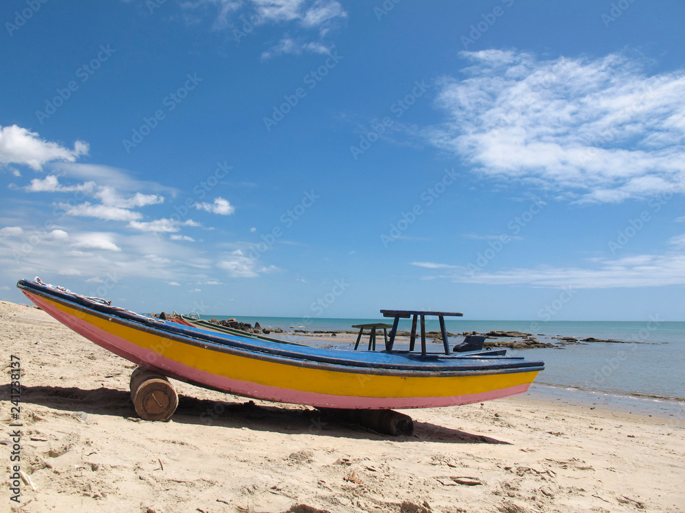 old wooden boat in blue and yellow colors, on white beach with blue sky - Fortaleza, Ceara, Brazil