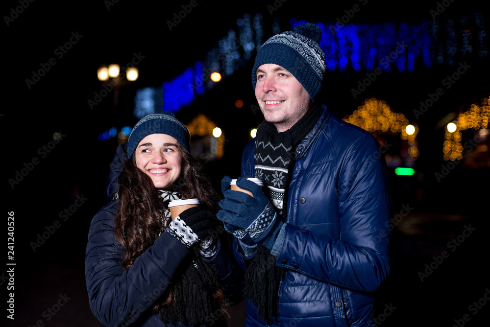 Winter holidays, hot drinks and people concept - happy young couple with coffee at christmas market in evening Winter holidays, hot drinks and people concept - happy young couple with coffee at christmas market in evening