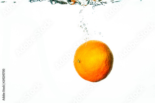Fresh orange falls into water with bubbles