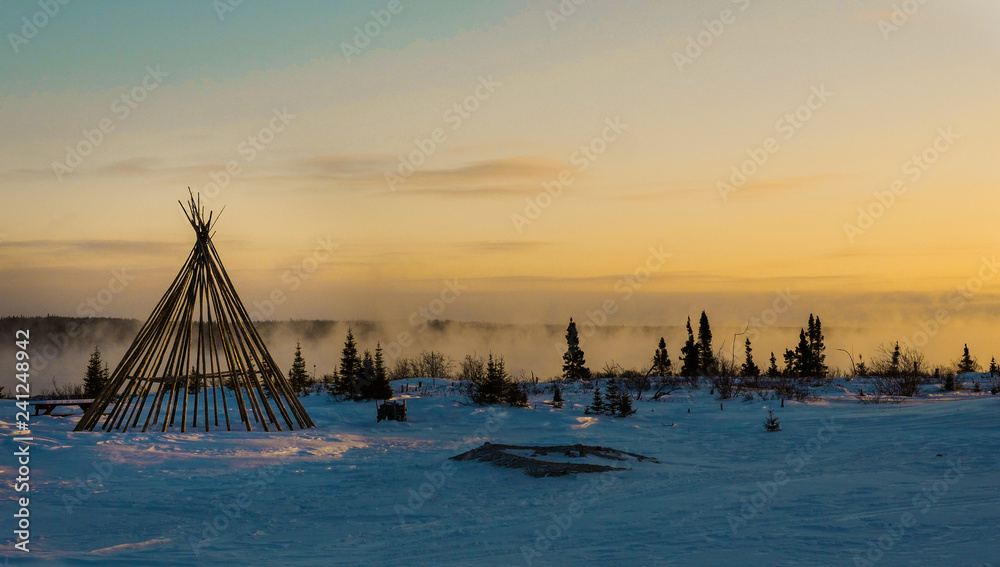 Fototapeta premium Cree tipi oprawione o zmierzchu nad mglistą rzeką w odległym północnym lesie borealnym Quebecu