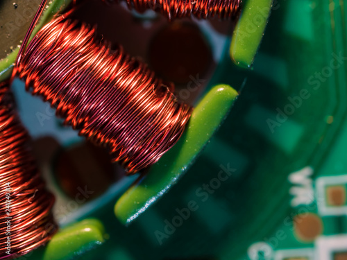 Red copper wire spooled on the steel core - a part of the electric engine placed on the green printed circuit board