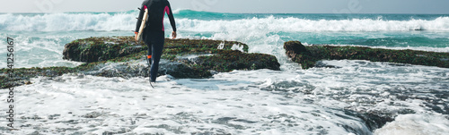 Woman surfer walking with surfboard on mossy coral reefs