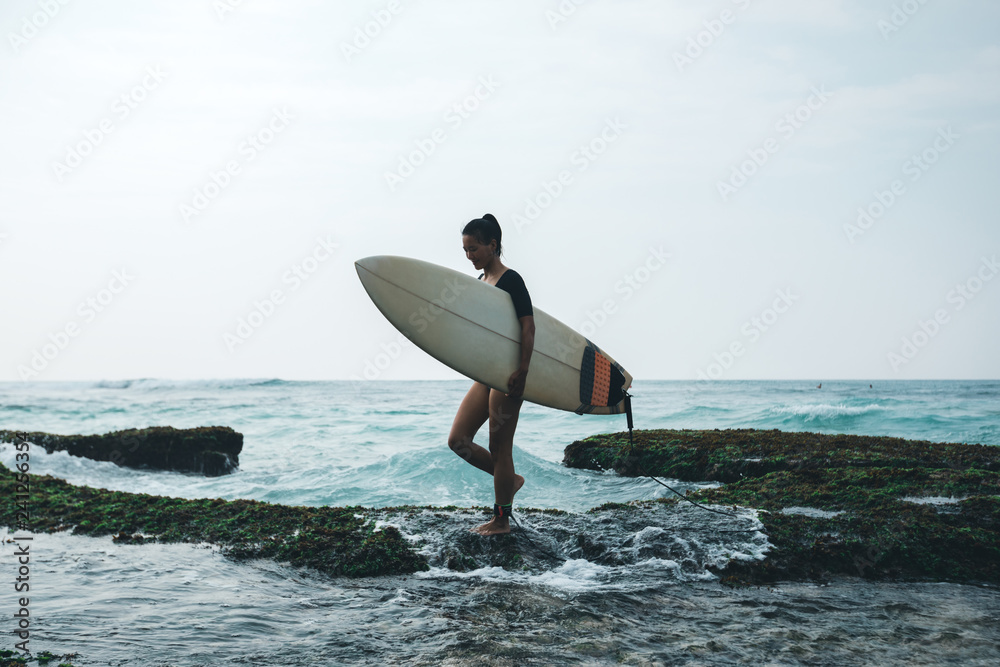 Woman surfer walking with surfboard on mossy coral reefs