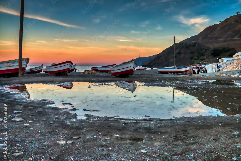 Dramatic sunset with boats reflecting in the water on the beach of Oued Laou, Chaouen province, Morocco