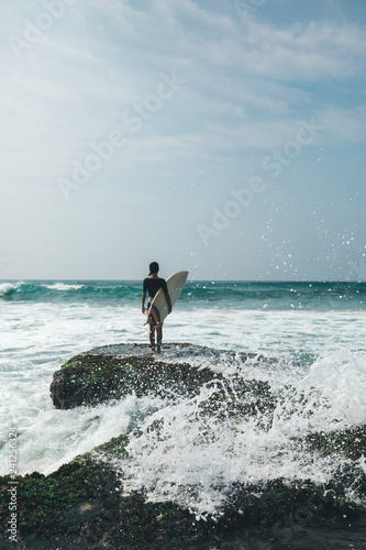 Woman surfer with surfboard on mossy seashore coral reefs
