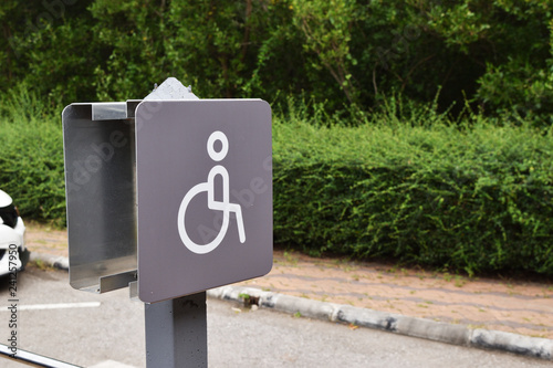 Disabled person parking sign with road and green tree in background