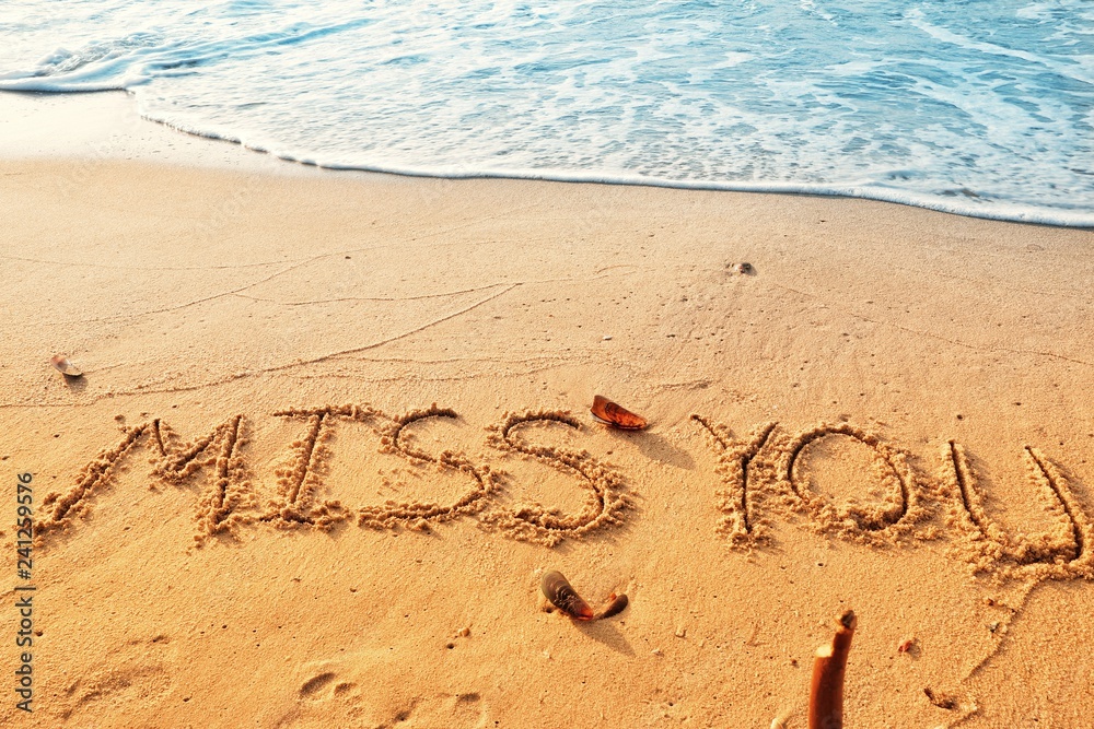 Fototapeta premium Valentine's day concept, miss you writing on sand beach with waves blue ocean.