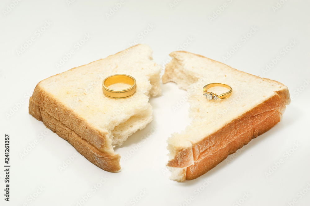 Two separate wedding rings with torn bread meaning to the word divorce.