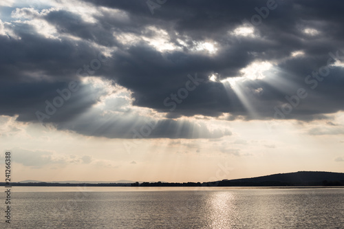 Beautiful sunset on a lake, with sunrays coming down under an overcast sky © Massimo