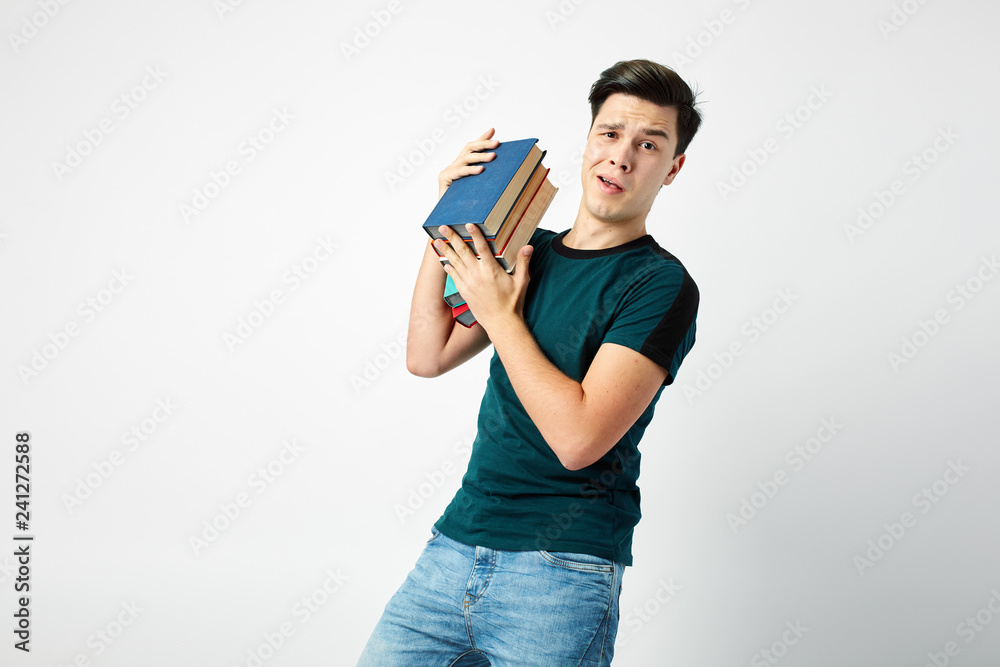 Funny dark-haired guy dressed in a dark t-shirt and jeans holds books on his shoulder on a white background Funny dark-haired guy dressed in a dark t-shirt and jeans holds books on his shoulder on a white background