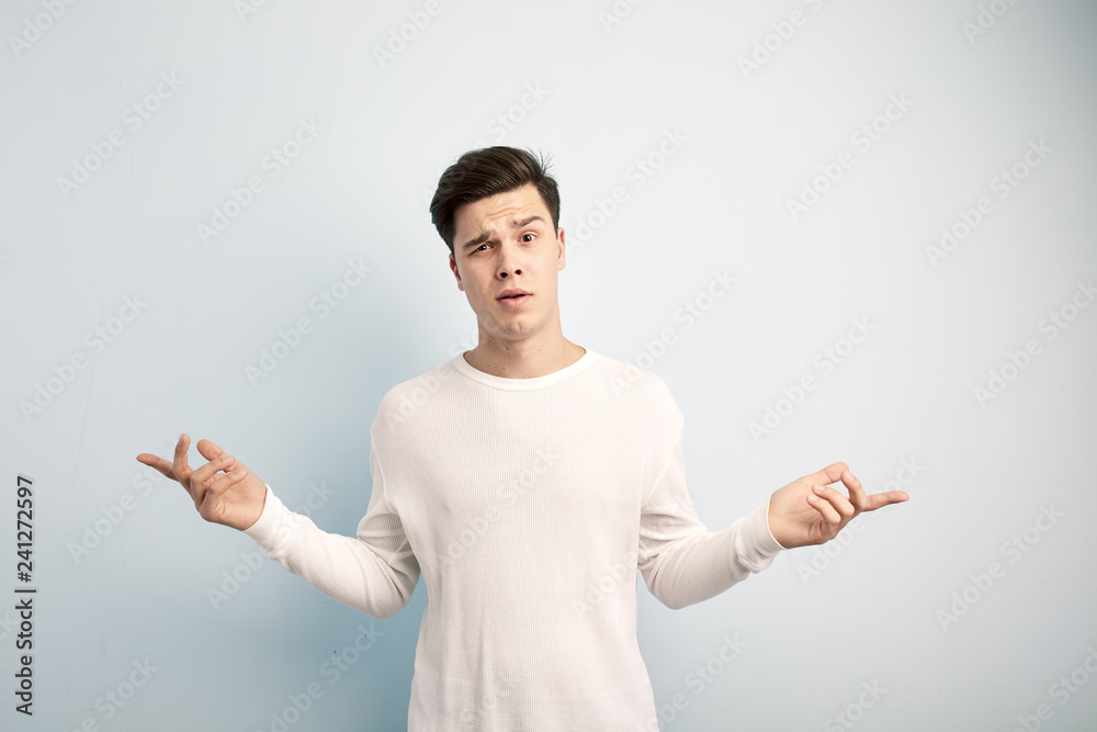 Surprised dark-haired guy dressed in a white long sleeve t-shirt and jeans stands on a white background Surprised dark-haired guy dressed in a white long sleeve t-shirt and jeans stands on a white background