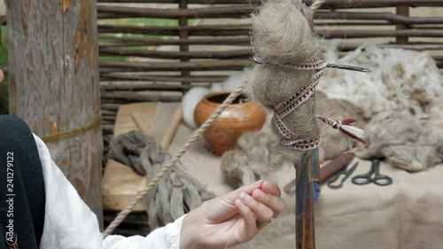 Reconstruction of medieval hand spinning. Spinner pulling out wool strand from unspun fibers secured on distaff