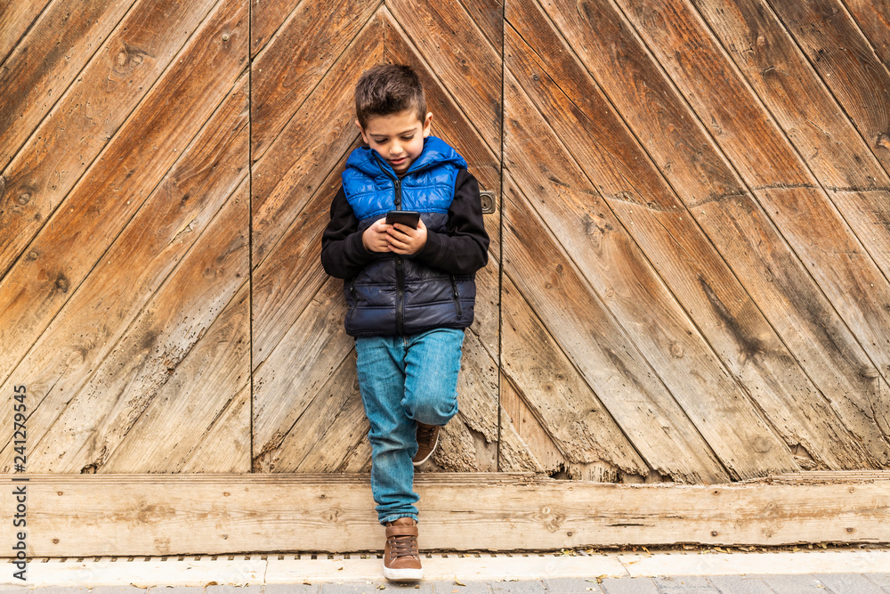 Little boy with a mibile phone with a wooden door background