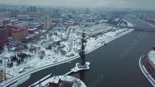 Drone flies over the Moscow River around the monument of Peter the Great. All buildings in the snow. Red October and Central House of Artists in shot. Winter. Overcast weather.