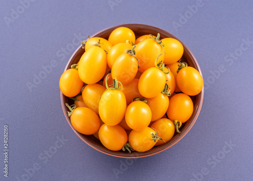 Fresh cherry tomatoes in a wooden bowl isolated on a blue background, close up, copy space photo