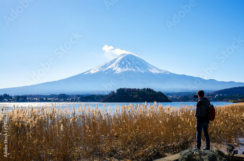 Photographer man standing outdoor photography by mobile amidst beautiful nature of Mt. Fuji at Yamanashi in Japan with lake kawaguchiko. Travel and Attractions Concept.