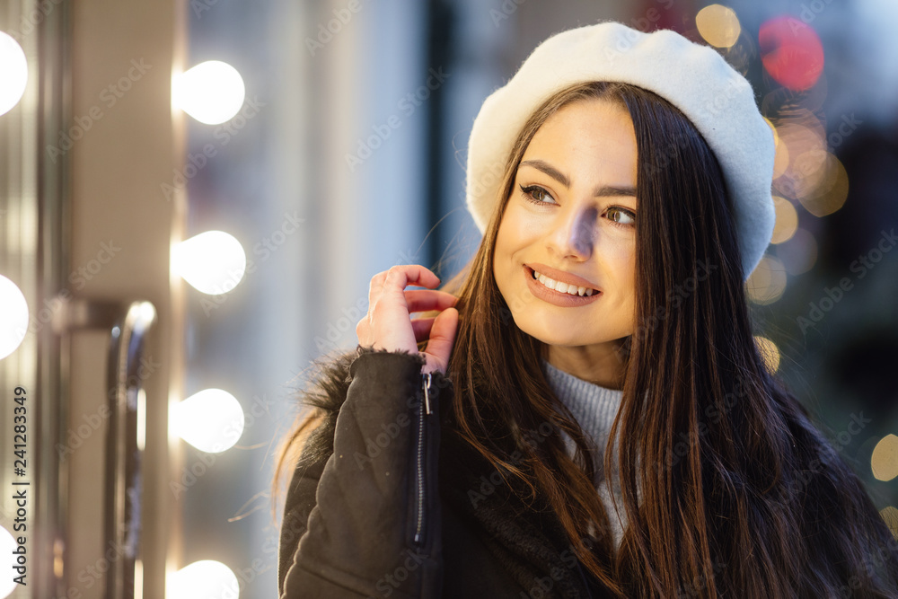 Fototapeta premium Pretty girl stand on the street wear black hat, look at window store and make funny expressions on her face. - Image