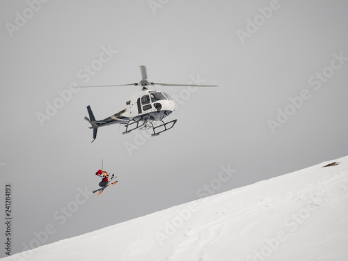 Skier freerider jumps from helicopter heliski on a snowy mountain photo