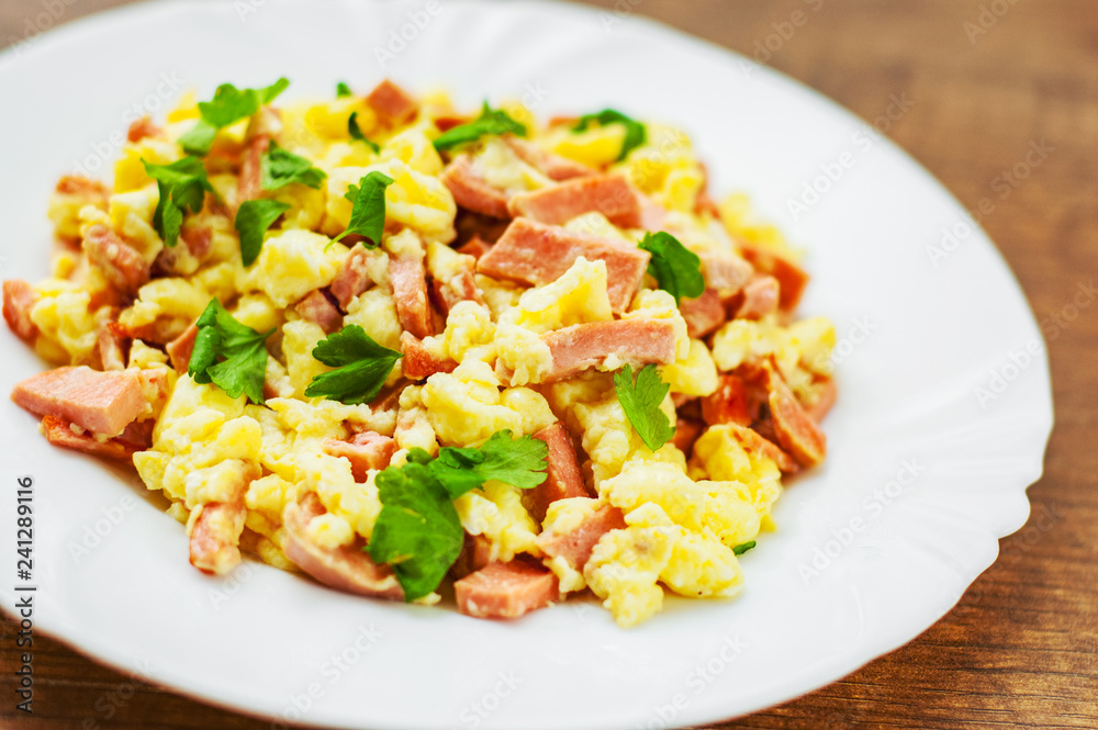 scrambled eggs with ham and cheese in white plate on wooden table background scrambled eggs with ham and cheese in white plate on wooden table background
