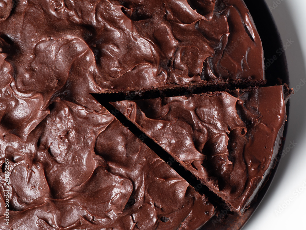 Overhead shot of a cut chocolate cake on a wooden plate and white background Overhead shot of a cut chocolate cake on a wooden plate and white background