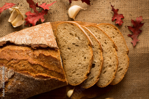  Pokorojony świeży chleb w kompozycji z jesiennymi liśćmi i czosnkiem.
