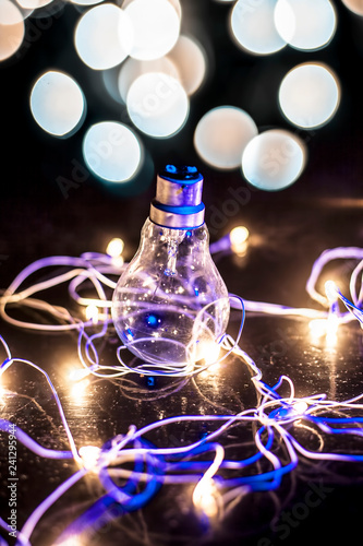 Close up of a bulb on wooden surface with colorful blurred background or bokeh of Christmas lights with it.